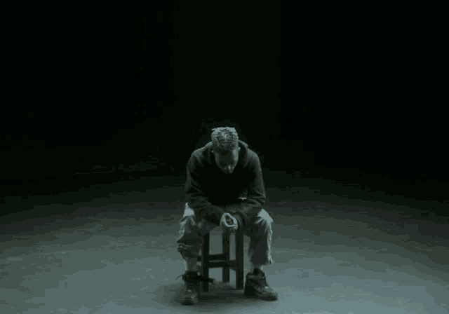 a man sits on a stool in front of a collage of pictures of rappers