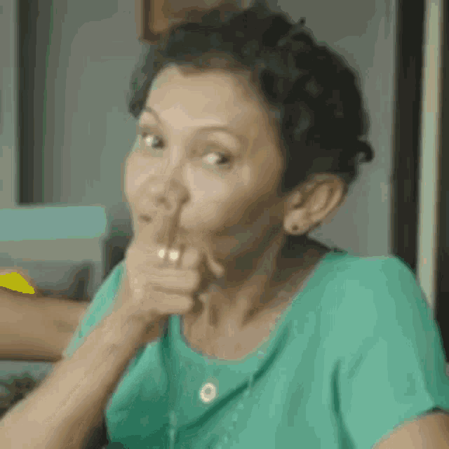 a woman in a green shirt is making a funny face and pointing her finger at the camera .