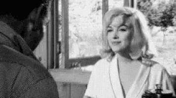 a black and white photo of a woman talking to a man in a room .