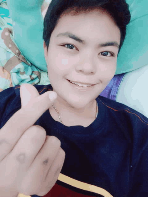 a young man is smiling and making a heart sign with his finger