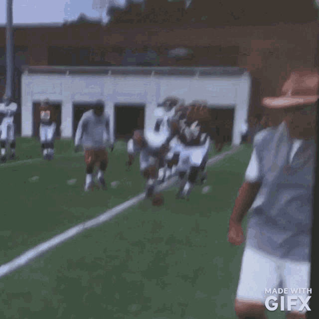 a group of football players are running on a field with a man in a cowboy hat