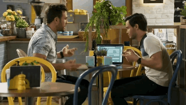 two men are sitting at a table with a laptop