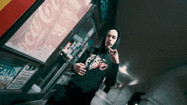 a man in a black hoodie stands in front of a coca cola sign