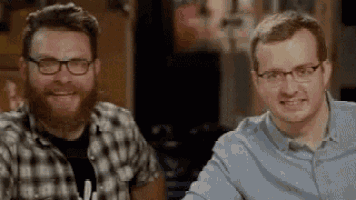 two men with beards and glasses are sitting next to each other at a table and smiling .