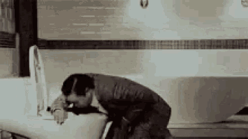 a man is sitting on a toilet in a bathroom with his head down .