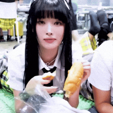 a girl with long black hair and a tie is eating a piece of food .