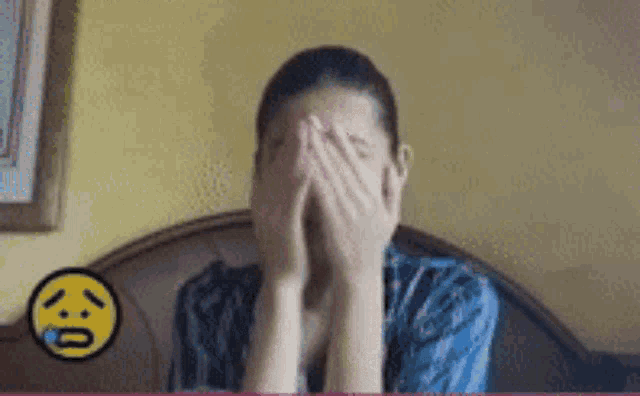a woman is covering her face with her hands and a smiley face is behind her .