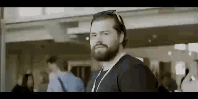 a man with a beard wearing sunglasses and a lanyard is standing in a crowded room .