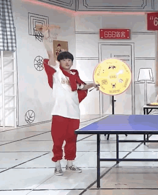 a young boy is playing ping pong in a room with a sign that says 6666