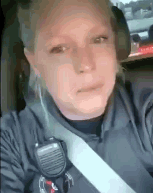 a woman in a police uniform is sitting in a car with a microphone on her neck .