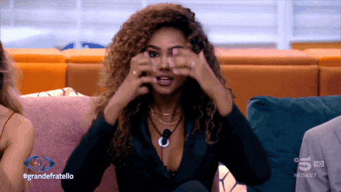a woman sitting on a couch with #grandefratello written on the screen