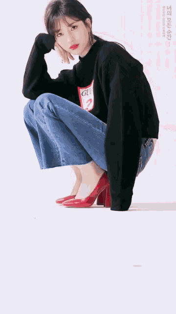 a woman is squatting down wearing a black sweater and jeans