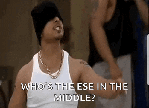 a man wearing a white tank top and a black hat is asking who 's the ese in the middle ?
