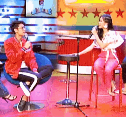 a man in a red jacket is talking into a microphone while a woman in pink pants is singing into a microphone