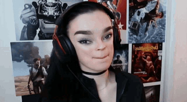 a woman wearing headphones and a choker is making a funny face in front of a wall with posters of video games