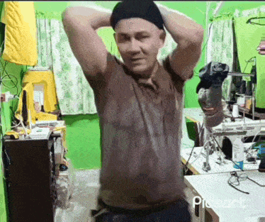 a man wearing a hat is standing in a room with his arms behind his head .