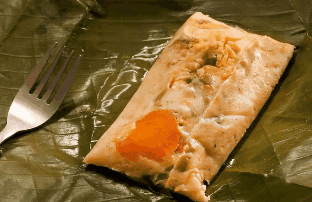 a piece of food with a carrot on it sits on a leaf next to a fork