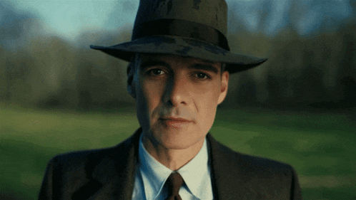a man wearing a hat and a suit is looking at the camera
