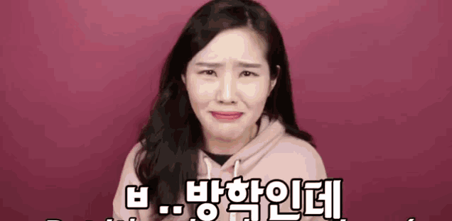 a woman is making a funny face in front of a red background while wearing a pink hoodie .