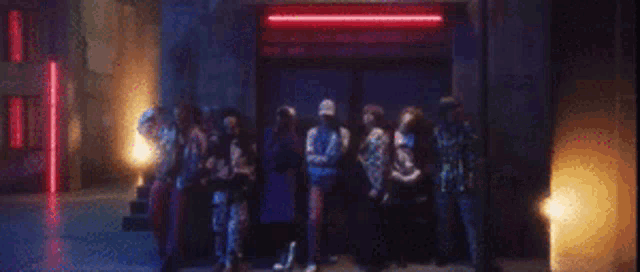 a group of people are standing in front of a building with a red light behind them .