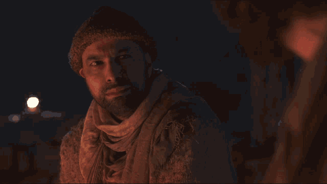 a man with a beard wearing a hat and scarf looks down