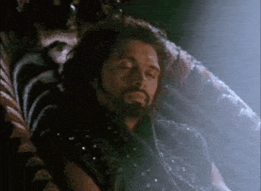 a man with a beard is sleeping in a chair with his eyes closed .