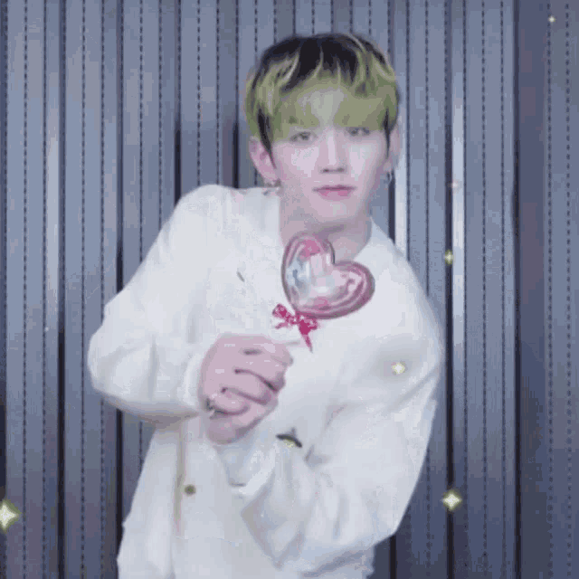 a young man with green hair is holding a heart shaped lollipop