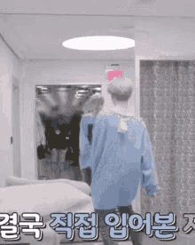 a man in a blue sweater is walking down a hallway with a red exit sign on the wall