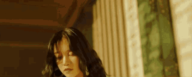 a woman with long dark hair is standing in a room with her eyes closed .
