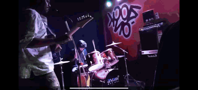 a man playing a guitar in front of a drum set with the word swan on it