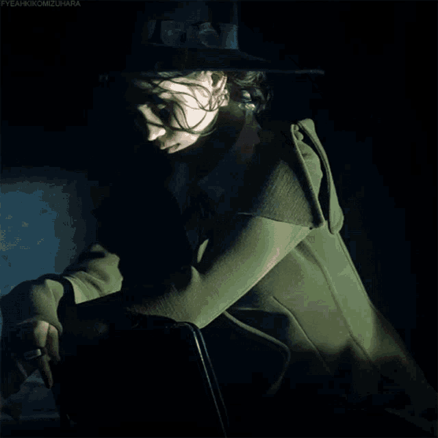 a woman wearing a black hat and a green coat is smoking a cigarette in the dark