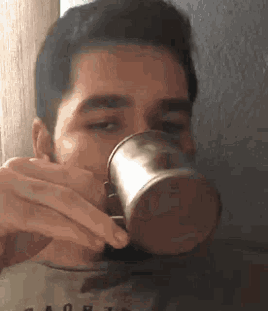a man with a beard is drinking from a metal mug .