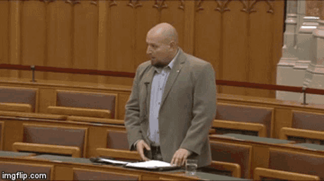 a man in a suit is giving a speech in a parliament and the word fuck is on the podium