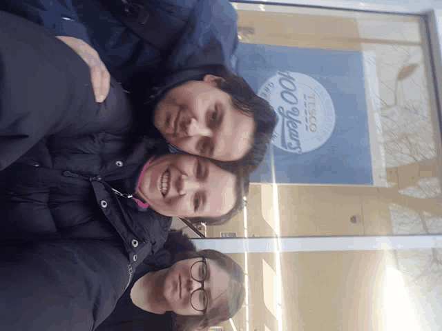 three people posing in front of a tesco sign