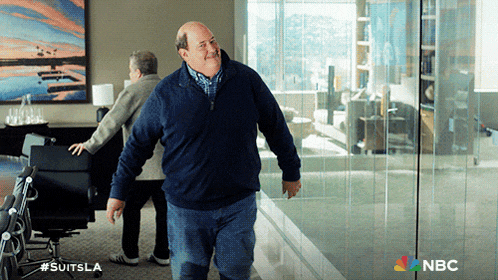 a man in a blue sweater is walking in a room with a nbc logo on the bottom right
