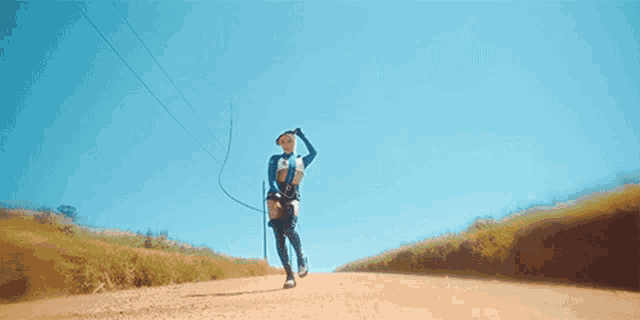 a woman is walking down a dirt road with a whip in her hand