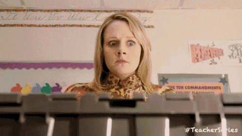 a woman is sitting in front of a keyboard in a classroom and making a surprised face .