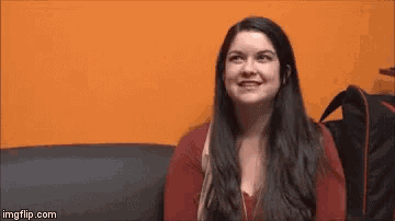 a woman is sitting on a couch smiling and looking at the camera .