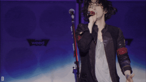 a man singing into a microphone with the letter d in the lower right corner