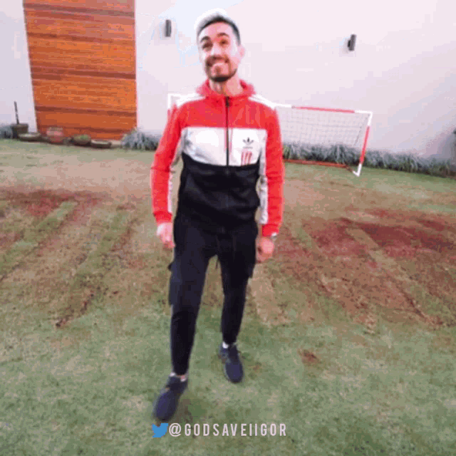 a man in a red white and black adidas jacket stands in a field