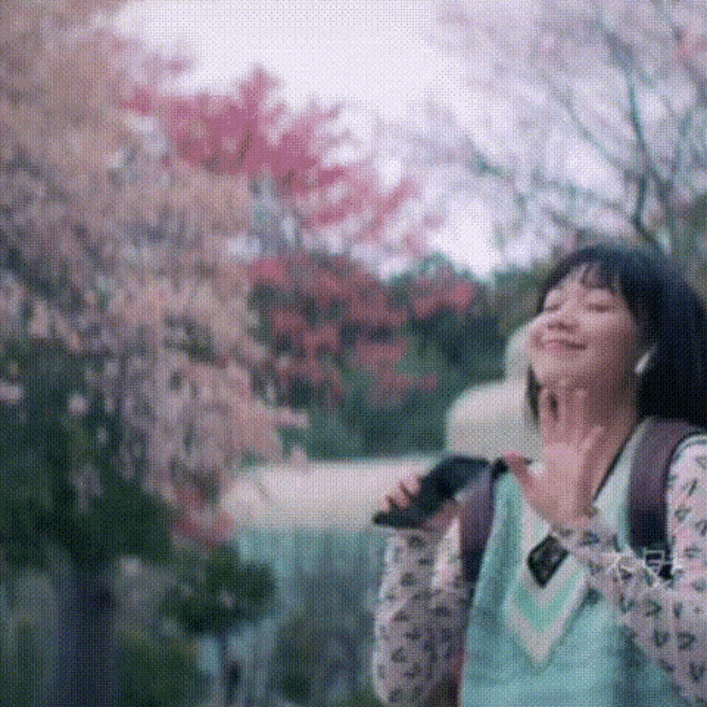 a woman with a backpack is talking on a cell phone in front of a cherry blossom tree .