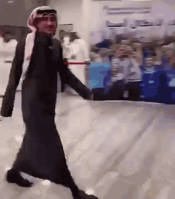 a man in a black robe and head scarf is walking in front of a crowd .