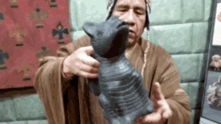 a man in a brown robe is holding a black statue of a monkey .