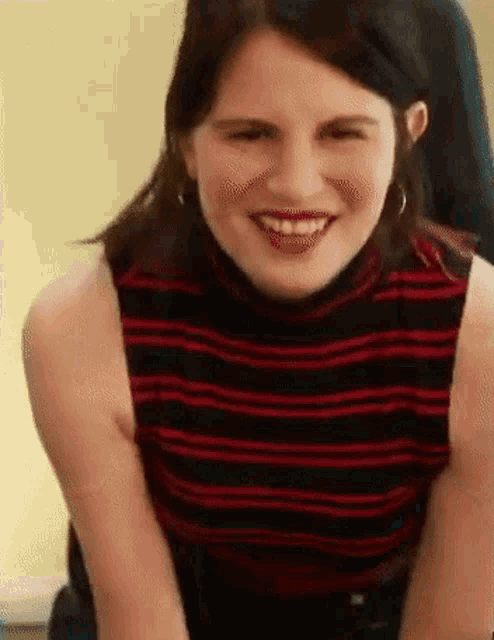 a woman in a red and black striped shirt is smiling and looking at the camera .