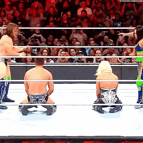 a group of wrestlers are kneeling down in a wrestling ring while a crowd watches .