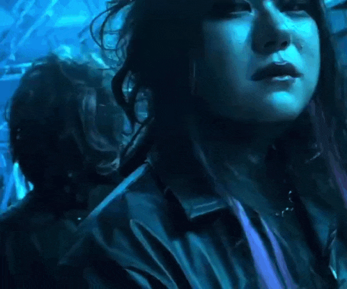 a close up of a woman 's face in a dark room with a blue light behind her .