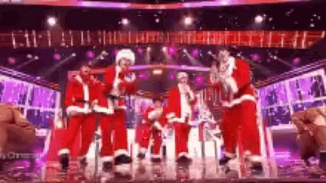a group of men dressed as santa claus are standing on a stage .