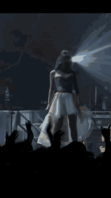a woman in a white dress stands on a stage with a fender amplifier in the background