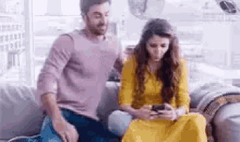 a man and a woman are sitting on a couch and looking at a cell phone .