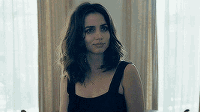 a woman in a black tank top is sitting in front of a window